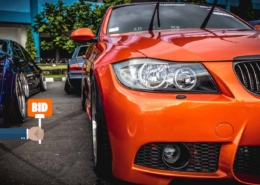 Orange BMW M Series up for bid at salvage car auctions, with potential buyers holding bidder paddles around the auction block.