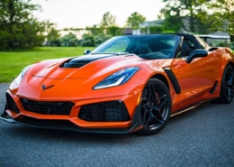 Vibrant orange Chevrolet Corvette speeding down a scenic road, available for bidding at an online auto auction.