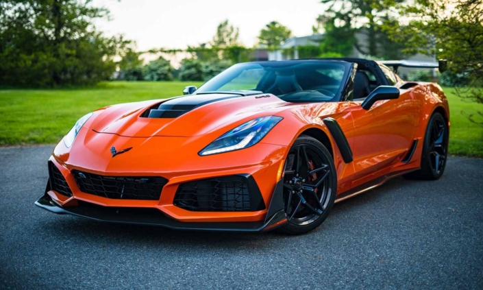 Vibrant orange Chevrolet Corvette speeding down a scenic road, available for bidding at an online auto auction.