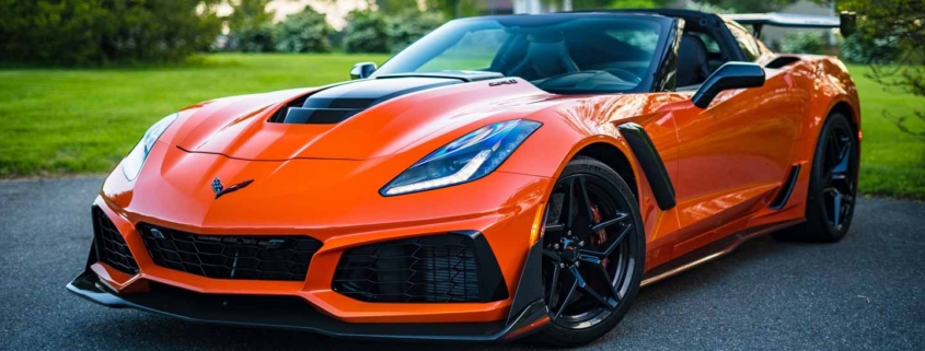 Vibrant orange Chevrolet Corvette speeding down a scenic road, available for bidding at an online auto auction.