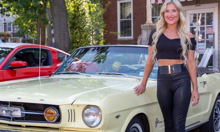 Woman proudly standing next to her classic Ford Mustang sports car