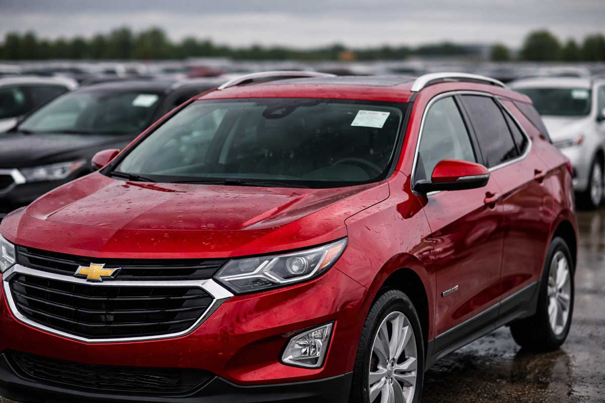 Red Chevrolet Equinox with hail damage dents on hood and roof parked at outdoor car auction lot